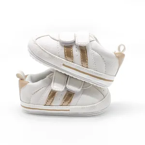 Side view of white baby walking shoes with gold double-stripe design and velcro straps.