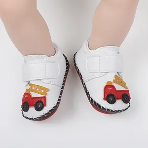 Gros plan de chaussures bébé blanches avec motif camion de pompiers et semelle cousue main.