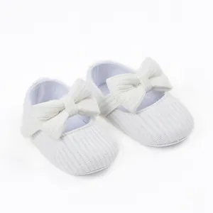 Detailed macro view of white ribbed soft-sole baby girl princess shoes with a large bow decoration