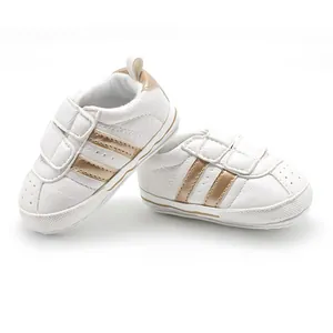 Detailed macro view of white baby walking shoes featuring two gold stripes and velcro