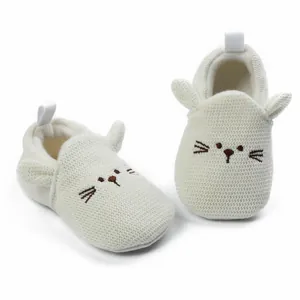 Close-up of white knitted infant walker shoes with cute cartoon cat face embroidery