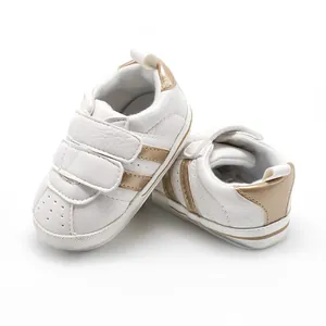 Detail view of white baby walking shoes featuring stylish gold stripes and velcro straps