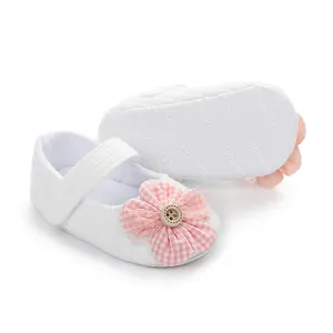 Detalle de zapatos blancos para bebé niña con adorno de flor de cuadros rosa.