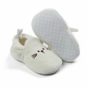 Detailed view of white knitted baby shoes with cute cat face and non-slip sole