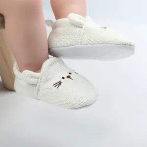 Close-up detail of white knitted baby walking shoes with cute embroidered cartoon cat face