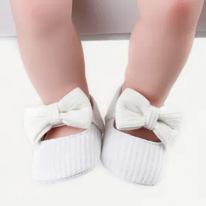 Close-up of soft knit baby girl walking shoes with a large white bow decoration.