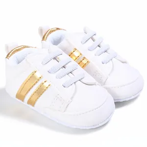 Vista lateral de zapatos de bebé blancos con rayas doradas y cordones elásticos suaves