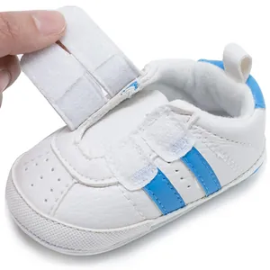 Detailed view of white baby sneaker with blue stripes and adjustable velcro closure strap