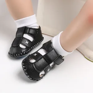 Nahaufnahme von schwarzen Baby-Sommersandalen mit weißem Kreuzstick und Klettverschluss.