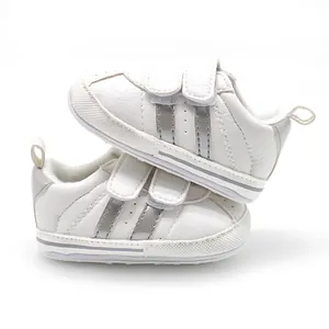Detailed view of white baby sneakers with silver double stripes and velcro straps.