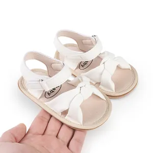 Detailed close-up of white infant sandals featuring a large bow and adjustable strap