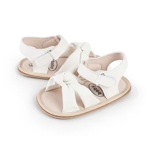 Macro detail of white infant walking shoes featuring a decorative knot and velcro strap.