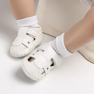 Nahaufnahme von weißen Baby-Sandalen aus Kunstleder mit Kreuzstich und Klettverschluss
