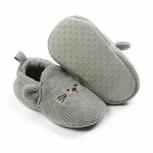 Detail of grey knitted baby shoes with cartoon cat face and non-slip sole texture