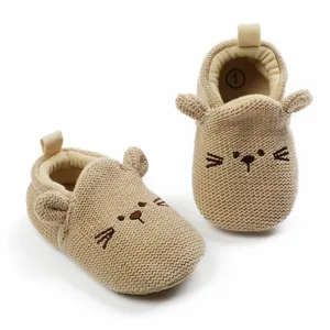 Close-up of beige knitted baby walking shoes with cute cartoon cat ears and face