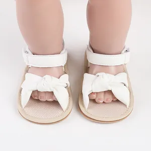 Detailed view of soft white infant walking sandals with large decorative knot bow design