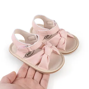 Detailed view of pink baby sandals with soft bow knot and velcro strap held in hand