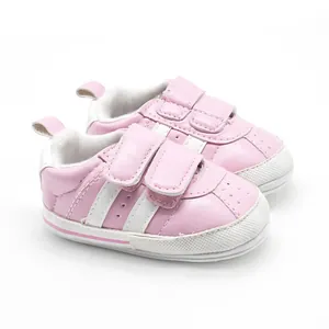 Detail of pink baby walking shoes featuring two white stripes and soft rubber soles
