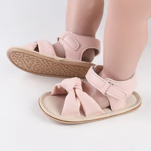Close-up of pink baby sandals with decorative bow and adjustable velcro strap for infants.