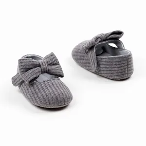 Close-up of grey knitted infant princess shoes with bow and velcro strap detail