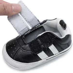 Detail view of the adjustable hook and loop strap on black infant walking shoe.
