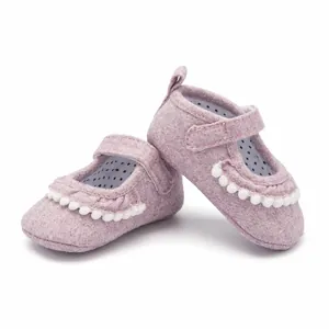 Nahaufnahme rosa Baby-Mary-Janes aus Stoff mit feinen weißen Pompon-Verzierungen und Details