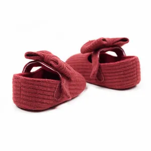 Macro detail of red knitted baby girl princess walking shoes with large bow decor.