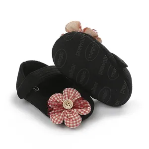 Primer plano de zapatos negros de bebé con una flor decorativa a cuadros rojos.