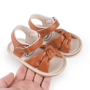 Detailed view of brown faux leather baby walker sandals with knot design held in hand