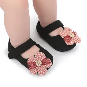Primer plano de zapatos de bebé niña negros con flor de cuadros rojos y botón central.