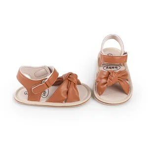 Macro view of brown faux leather baby sandals featuring a bow-knot and ankle strap