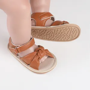 Close-up of brown faux leather baby walking sandals with knot detail and soft sole.