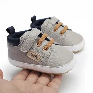 Macro view of grey textured baby walking shoes with Baby Boy patch held in hand for scale