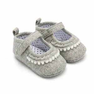 Λεπτομέρεια από γκρι υφασμάτινα παπούτσια μωρού με λευκά πομ-πομ και μαλακή σόλα.