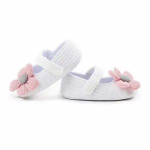Detailed view of white ribbed knit baby walking shoes with pink and grey fabric flowers