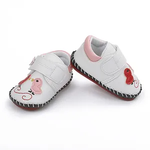 Vista detallada de zapatos de bebé blancos con detalles rosas y diseño de pájaro.