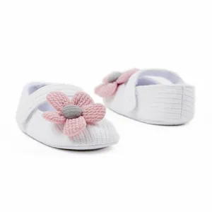 Detailed view of cute white knitted baby girl toddler shoes with a pink flower decoration