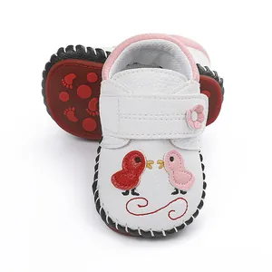 Vista detallada de zapatos de bebé blancos con bordado de pájaros y detalles en rosa
