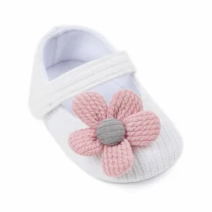 Close-up of a white knitted baby walker shoe with a large pink fabric flower detail