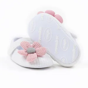 Macro detail of white knitted baby pre-walker shoes featuring pink flower and soft sole