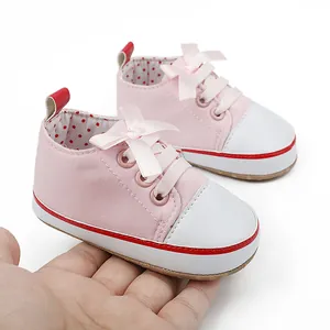 Close-up view of a pink baby girl pre-walker shoe with a ribbon bow held in hand