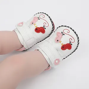 Primer plano de zapatos de bebé blancos con bordados de dibujos animados y cierre rosa.