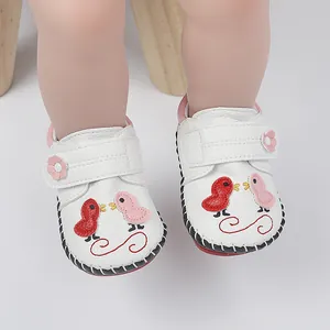 Detalle de zapatos blancos para bebé con bordado de pájaros y cierres de velcro.