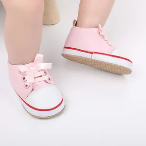 Close-up of pink baby girl walking shoes featuring ribbon laces and white toe caps.