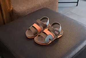 Detailed view of brown children's sandals with orange and blue straps on a textured surface