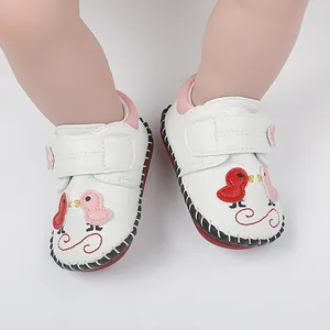 Detalle de zapatos de bebé blancos hechos a mano con bordado de pájaros y detalles rosas
