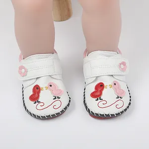 Detalle de zapatos blancos para bebés con bordado de pajaritos y cierre de velcro