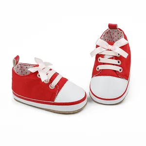 Close-up of red canvas baby pre-walker shoes with pink satin bows and soft white soles