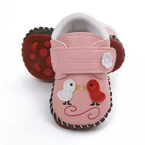 Detalle de zapatos de bebé rosa con bordado de pájaros de dibujos animados y flores.