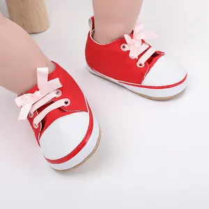 Close-up view of red infant walking shoes featuring pink ribbon laces and white toe caps